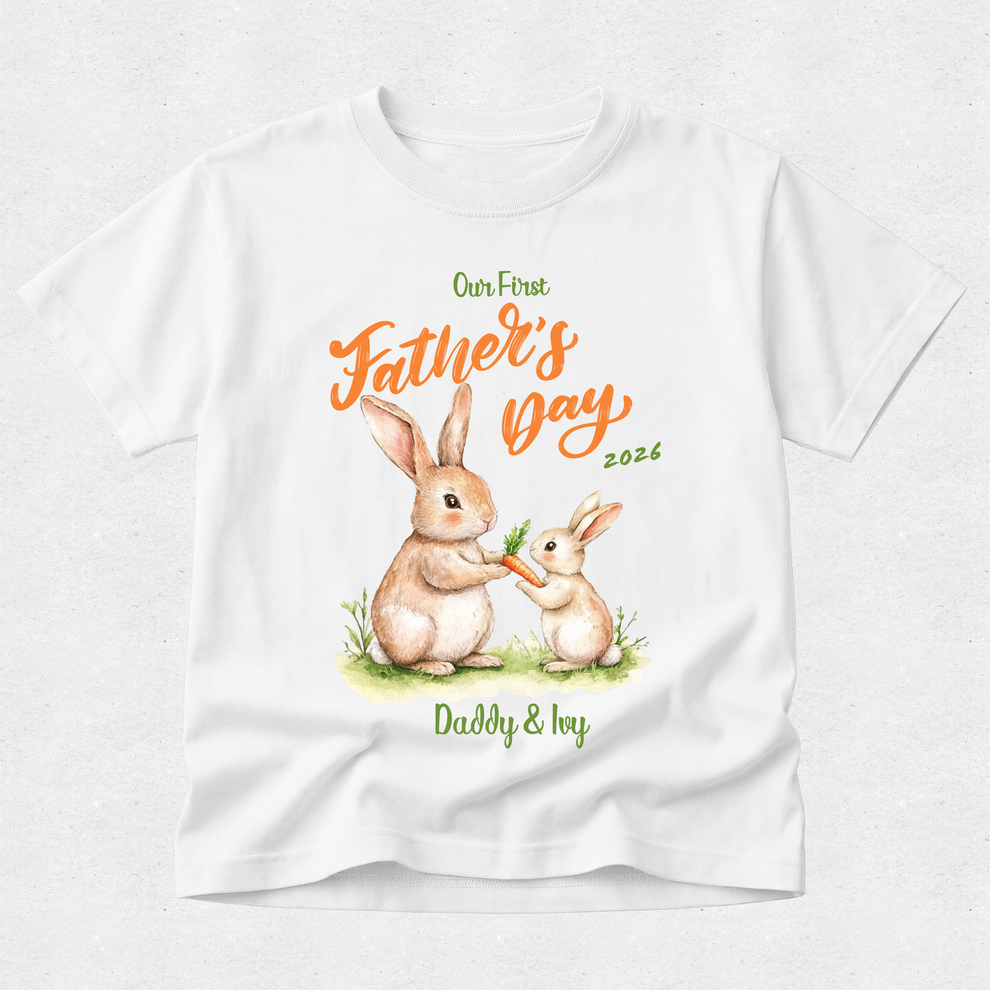 A white short-sleeve t-shirt with a custom Father's Day graphic featuring a watercolor illustration of a mother rabbit and her baby, with orange and green text reading 'Our First Father's Day 2026' and 'Daddy & Ioy'.