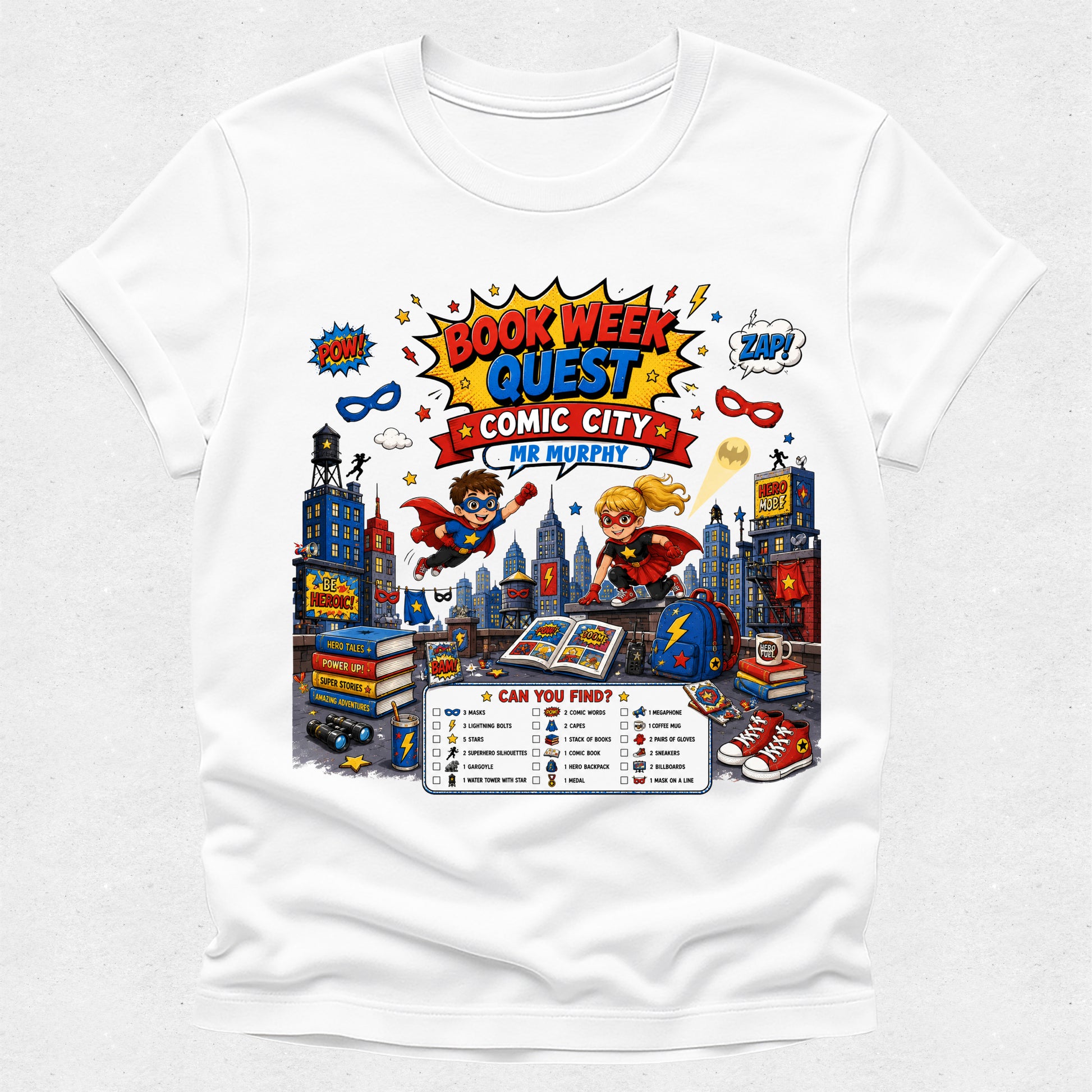 A white short-sleeve crewneck t-shirt featuring a colorful graphic print on the front. The graphic is themed around 'Book Week Quest Comic City' and includes illustrations of superheroes, comic books, a cityscape, and a checklist.