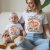 Woman and baby sitting on a couch wearing matching 'First Mother's Day Together' shirts.
