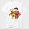 A white short-sleeve crewneck t-shirt featuring a colorful cartoon graphic of a father and daughter dressed as superheroes, with 'Happy Father's Day' text and the names 'Emma' and 'Daddy' printed below.