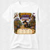 A white short-sleeve crewneck t-shirt featuring a colorful graphic print of a wizard character in a hat with a magnifying glass, surrounded by a magical library scene with the text 'BOOK WEEK QUEST WIZARD ACADEMY NAVY'.