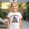 Child wearing a white t-shirt with a cartoon character and Easter text, smiling outdoors.
