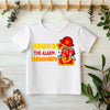 White t-shirt with fire-themed design and text on a light wooden surface with plants.