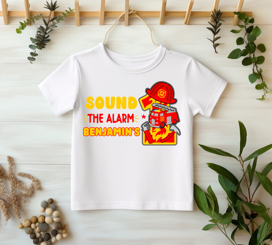 White t-shirt with fire-themed design and text on a light wooden surface with plants.