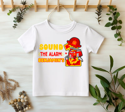 White t-shirt with fire-themed design and text on a light wooden surface with plants.