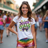 Woman wearing a 'Mardi Gras' shirt and colorful shorts in a busy street.