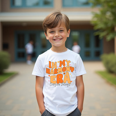 Child wearing a white t-shirt with orange text standing in front of a building.
