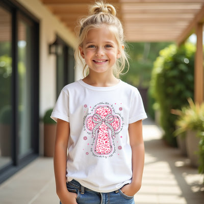 Young girl wearing a white t-shirt with a pink floral cross design outdoors.