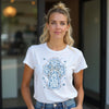 Woman wearing a white t-shirt with a blue cross design outdoors.