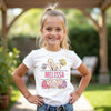 Young girl wearing a white t-shirt with 'Melissa' and Easter-themed graphics outdoors.