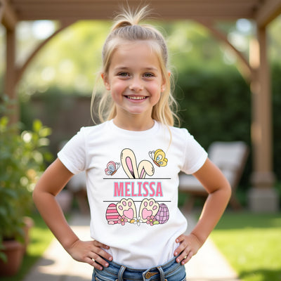 Young girl wearing a white t-shirt with 'Melissa' and Easter-themed graphics outdoors.