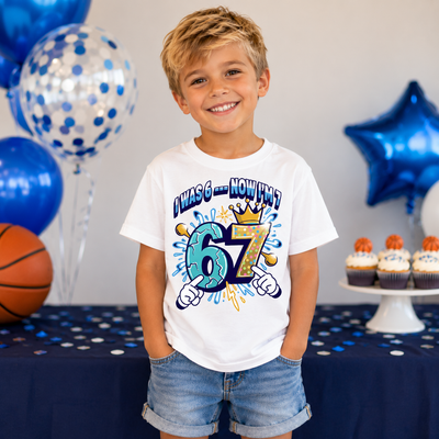 Boy celebrating his 7th birthday wearing colourful "I Was 6 Now I'm 7" birthday t-shirt with fun cartoon number design.