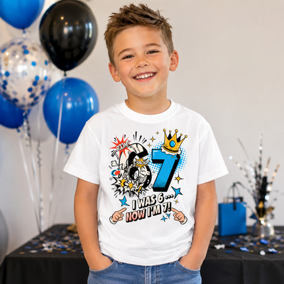 Boy wearing personalised 7th birthday t-shirt at a birthday party featuring "I Was 6... Now I'm 7!" comic design.